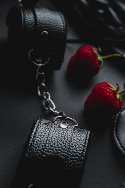 Black leather cuffs and fresh strawberries placed on a dark surface for a moody composition.
