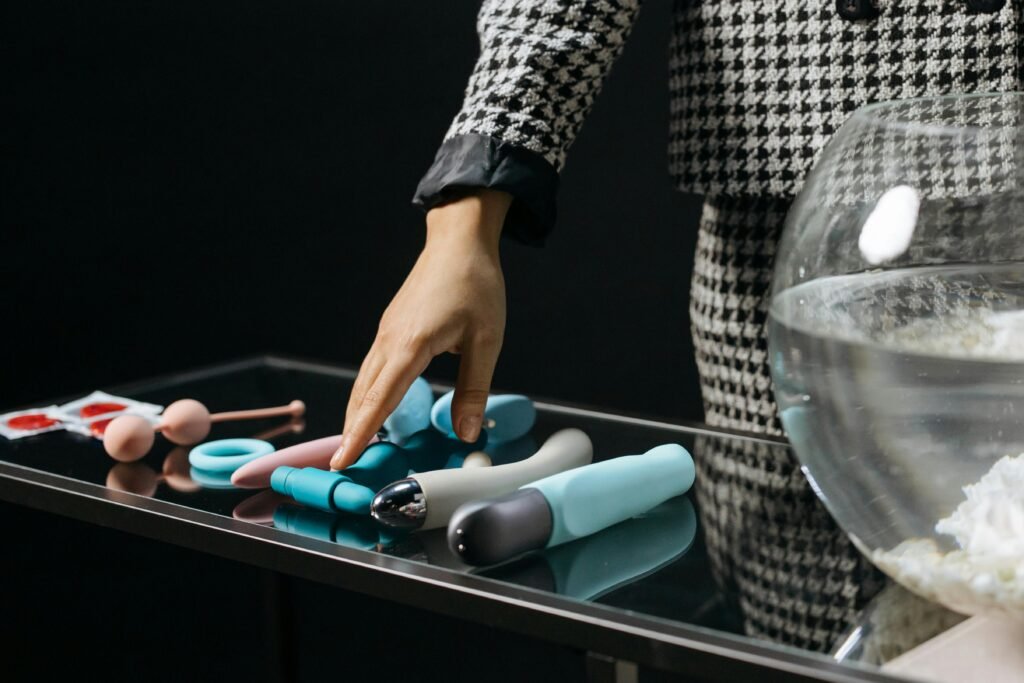 Hand reaching for various colorful silicone adult toys on a reflective glass table. Sensual and vibrant.