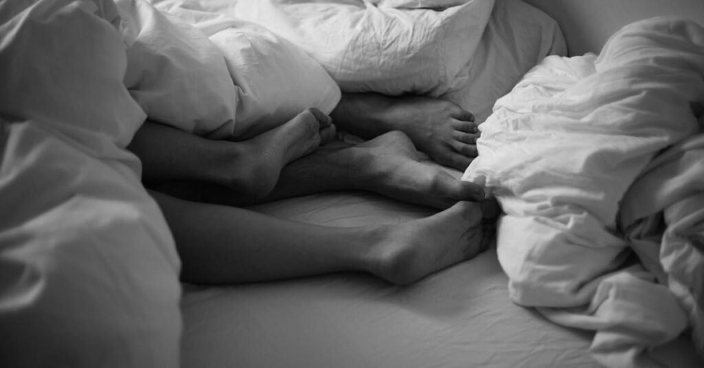 Black and white image of feet intertwined under cozy bedsheets, capturing a peaceful moment.