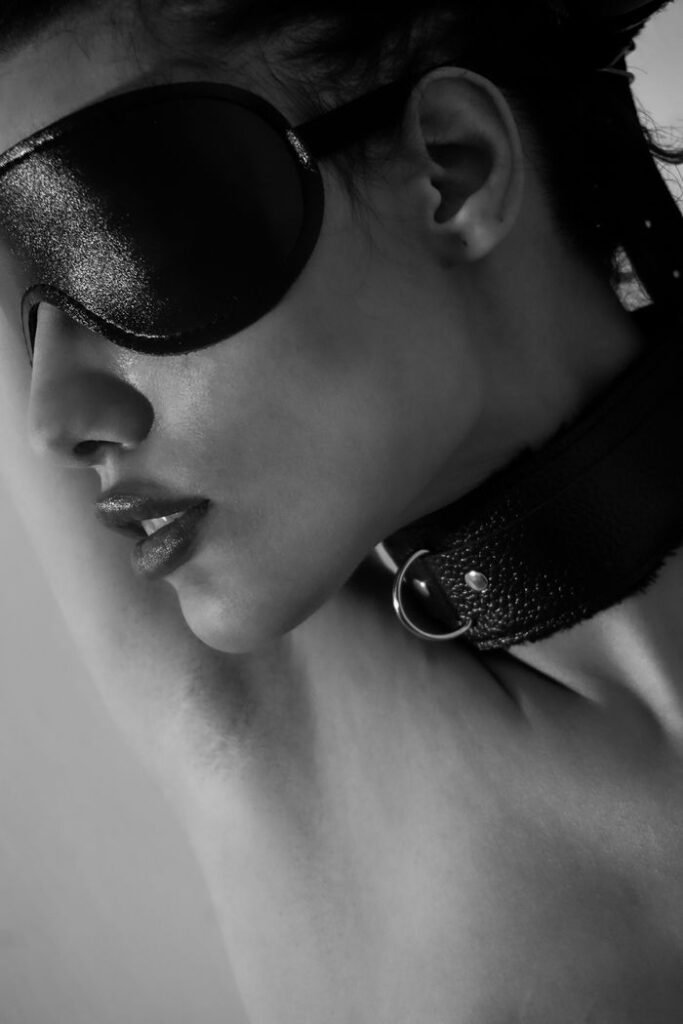 Black and white portrait of a blindfolded woman wearing a leather collar, conveying artistry and emotion.